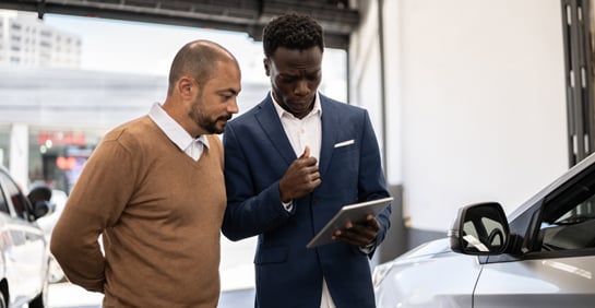 Two men reviewing data on a tablet while standing next to a car